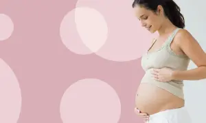 Uśmiechnięta kobieta w ciąży dotyka brzucha. Waga dziecka w 27 tygodniu ciąży jest już znacząca.