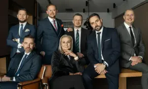 Grupa siedmiu profesjonalistów w garniturach, w tym jedna kobieta, pozuje do zdjęcia.