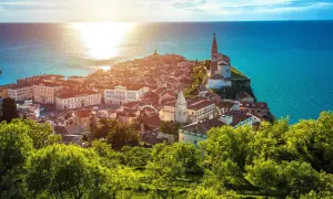 Sonnenuntergang über der malerischen Piran Altstadt, mit ihren roten Dächern und der Kirche, die auf einer Landzunge ins türkisfarbene Meer ragt.