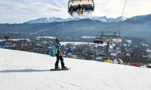 Snowboardzista na stoku, w tle kolejka krzesełkowa i góry. Zastanawiasz się, ile kosztuje karnet na narty?