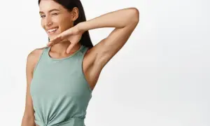 Mujer guiña un ojo y se rasca la axila, como si le picara. Su brazo está levantado, mostrando su piel suave.
