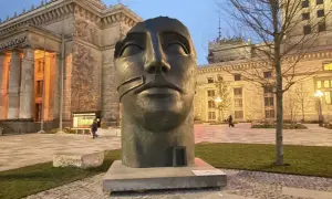 Głowa rzeźby Igora Mitoraja "Luci di Nara" na tle Pałacu Kultury i Nauki w Warszawie.