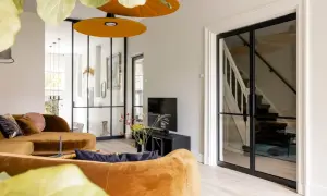 Luxe vestibule woning met oranje bank, glazen deuren naar de trap en een tv-hoek.