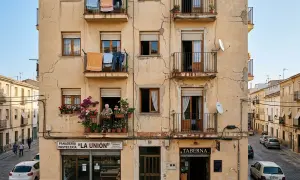 Edificio con fachada exterior agrietada, ropa tendida en balcones y una anciana cuidando flores. Necesita reparar fachada exterior.