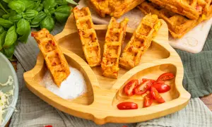 Leckere Pizza-Waffeln mit Mais und Paprika, serviert auf einem Kinder-Teller mit Tomaten und Dip. Ein Hit für kleine Feinschmecker!