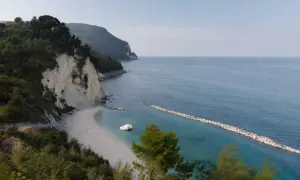 Scogliera verdeggiante e spiaggia bianca a Numana, con il lungomare che si estende verso il mare azzurro.