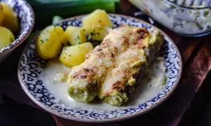Gebackener Lauch mit Schinken, überbacken mit Käse, serviert mit Salzkartoffeln und einer cremigen Sauce.