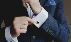 Mann schließt Manschettenknöpfe an seinem weißen Hemd. Was ist eine Manschette? Ein elegantes Detail für den Anzug.