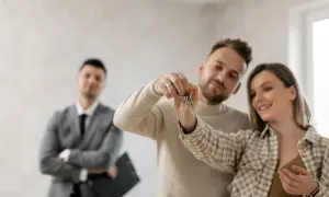 Coppia felice riceve le chiavi di casa, con un agente immobiliare sullo sfondo. Ottima opportunità per la surroga mutuo INPS dipendenti pubblici.