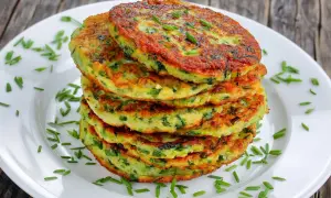 Pile de galettes de courgette dorées, parsemées de ciboulette fraîche sur une assiette blanche. Un délice végétal.