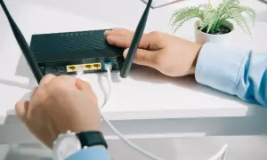 Mężczyzna podłącza kabel do czarnego rutera z dwiema antenkami.