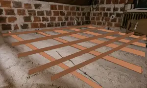 Nowa podłoga z płyt OSB na starych legarach, przygotowywana w nieukończonym pomieszczeniu z ceglanymi ścianami.