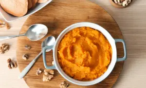 Un bol de purée de patate douce onctueuse, garni de noix et accompagné de tranches de patate douce.