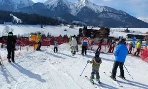 Ludzie na nartach i snowboardach w słoneczny dzień w ski centrum Strachan, z majestatycznymi ośnieżonymi górami w tle.