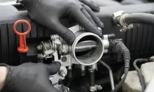 Mechanik w czarnych rękawiczkach sprawdza przepustnicę. Objawy jej awarii mogą być różne, np. nierówna praca silnika.