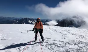 Une alpiniste, équipée pour l'ascension d'une montagne, se tient sur un sommet enneigé, le regard tourné vers l'horizon.