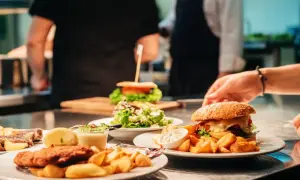 Pyszne jedzenie w restauracji: burgery, frytki, sałatka i kotlet. W tle kucharze przygotowują kolejne dania.