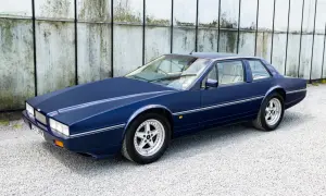 Granatowy Aston Martin Lagonda z lat 80. na tle industrialnej ściany.