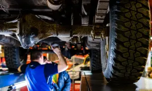 Mechanik sprawdza podwozie terenowego auta z napędem **awd**. Widoczna jest masywna oś i bieżnik opony.