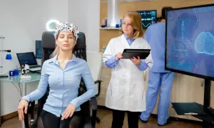 Kobieta w czepku EEG siedzi, lekarz z tabletem obserwuje ekran z analizą mózgu.