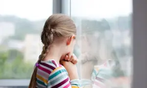Smutna dziewczynka z warkoczem patrzy przez okno. Czuje się samotna, bo dzieci nie chcą się bawić z moim dzieckiem w szkole.
