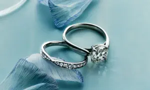Dos anillos de compromiso, uno con un gran diamante y otro con pequeñas gemas, descansan sobre pétalos de flor azul. Un anillo casado para siempre.