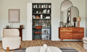 Un bureau placard aménagé avec une chaise orange, des étagères remplies de livres et un papier peint tropical.