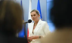 Minister edukacji przemawia przy mikrofonie, w tle flagi Polski i UE.