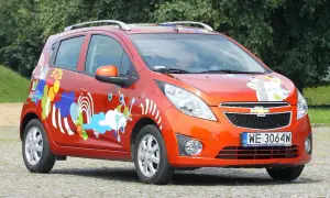Pomarańczowy Chevrolet Spark 2010 z kolorowymi, abstrakcyjnymi wzorami na karoserii.