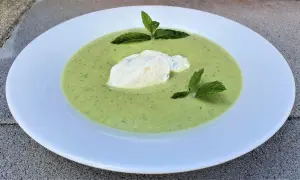 Velouté de courgette onctueux, garni d'une quenelle de fromage frais et de feuilles de menthe, servi dans une assiette blanche.