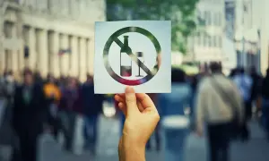 Dłoń trzyma kartkę z symbolem zakazu sprzedaży alkoholu po 22. Tło to rozmyty tłum ludzi na ulicy.