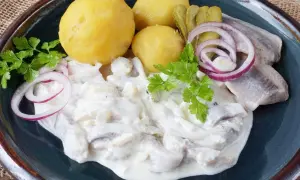 Marinierter Hering in cremiger Sauce mit Salzkartoffeln, Gurken und Zwiebelringen garniert.
