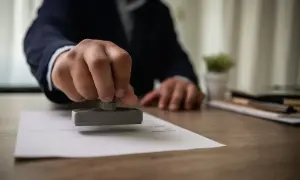 Dłoń z pieczątką nad dokumentem, finalizując formalności związane ze spadkiem po rodzicach.
