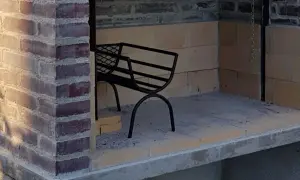 En påbörjad grill av tegelstenar med en svart metallbänk inuti.