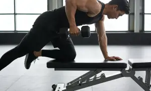 Homme en tenue de sport noir effectuant un rowing haltère sur un banc de musculation, bras tendu, concentré.