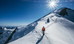 Un alpiniste solitaire progresse sur une crête enneigée, le soleil éclatant au-dessus du sommet du Mont-Blanc.