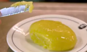 Un trozo de alioli casero untado en un cuchillo, listo para probar la deliciosa salsa sobre un plato blanco.