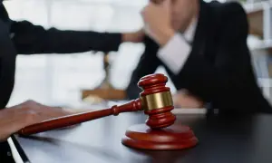Młotek sędziowski na stole. Dłoń kładzie się na ramieniu zmartwionego mężczyzny, sugerując, że prawa dłużnika ważniejsze niż wierzyciela.