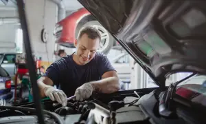 Mechanik w rękawiczkach naprawia silnik samochodu pod otwartą maską.
