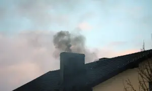 Ciemny dym wydobywa się z zimnego komina na tle błękitnego nieba z chmurami.