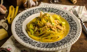 Pyszny kurczak curry z makaronem tagliatelle, podany na talerzu z ozdobnym wzorem. Obok czosnek i ser.