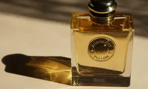 Złota butelka perfum Burberry Goddess, lśniąca w świetle, z wytłoczonym logo.