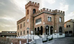 Edificio in mattoni rossi con torre dell'orologio e merlature, un esempio di cosa vedere a Mondolfo.