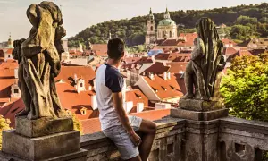 Un homme contemple les toits de Prague, une ville d'Europe aux charmes intemporels, depuis un balcon orné de statues.