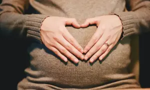 Mani a cuore sul pancione, simbolo di maternità flessibile e amore in attesa.