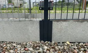 Metalowy łącznik słupka ogrodzenia do betonowej podmurówki. Kamienie ozdobne wokół.