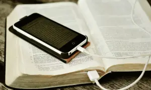 Nowoczesna biblia na co dzień: smartfon z tekstem biblijnym leży na otwartej księdze, podłączony do ładowania.