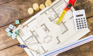 Plan mieszkania, miarka, kalkulator, kostki z cyframi i linijka na drewnianym tle.