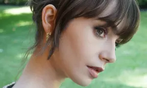 Kobieta z **baby bangs** i delikatną biżuterią w uchu, na tle zieleni.
