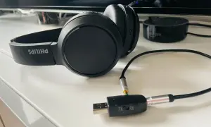 Czarne słuchawki Philips podłączone do adaptera Bluetooth TX/RX na białym blacie.